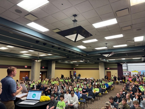 auditorium full of students seated and listening to a man give a presentation from behind a podium on a short stage