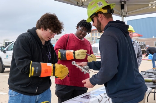 a mechanic shows to high school boys how to use wrenches with large PPE gloves on